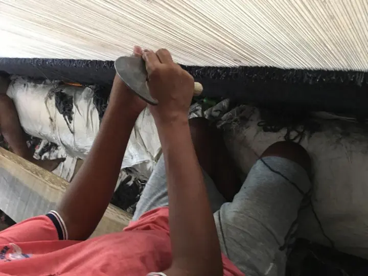 Weaver tying knots by hand at the loom on a custom rug